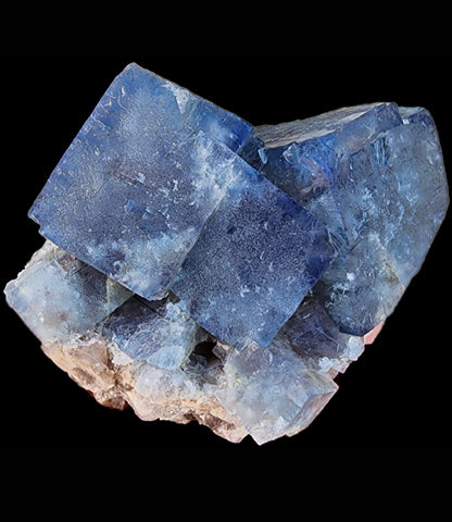 A cluster of cubic blue Fluorite- Fairy Holes Pocket crystals from the famed Lady Annabella Mine in Eastgate, Weardale, Co. Durham, England, is shown against a solid black background. The translucent crystals exhibit varying shades of blue with some white inclusions, creating a striking and intricate mineral formation. This stunning piece is featured by The Crystalary.