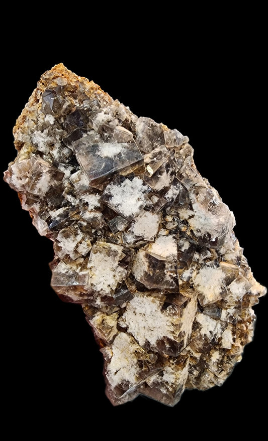 A cluster of brown and white mineral crystals, identified as Fluorite from the Smoky Rabbit Pocket at the Diana Maria Mine in Frosterley, Weardale, Co. Durham, England, stands out against a black background. These crystals from The Crystalary display a shiny surface with an array of shades and geometric patterns that echo Weardale's distinctive mineral formations.