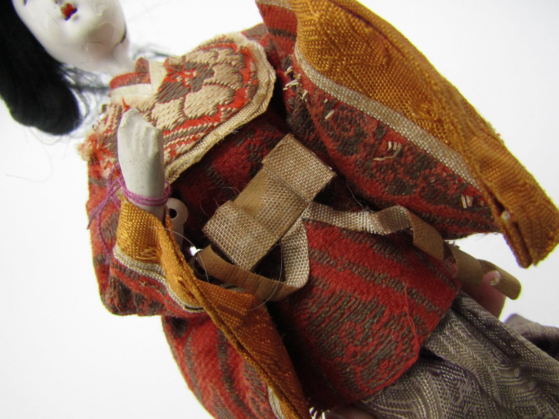 A close-up view of The Crystalary's Antique Japanese Ningyo Doll, a 7" early to mid-20th century Asian doll, adorned in an intricate kimono featuring red, orange, and gold patterns. The doll's head is slightly tilted, with black hair and a serene expression, showcasing the detailed craftsmanship of its attire.