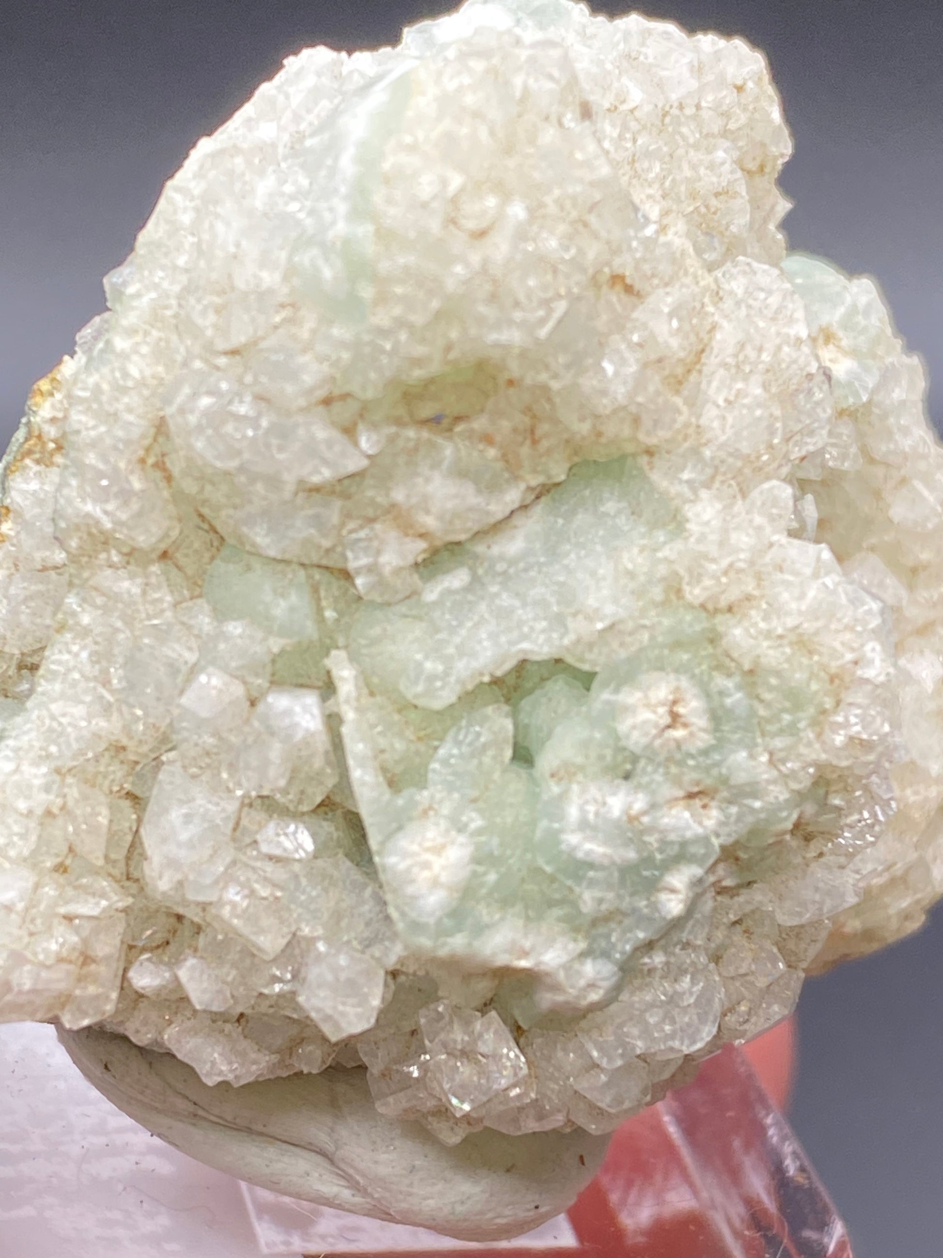 Close-up of a pale green, translucent mineral specimen, presumably Apophyllite on Prehnite from The Crystalary, showcasing a rough, crystalline texture. This exquisite piece from the O & G Woodbury Traprock Quarry in Orenaug Hills is elegantly displayed on a small pedestal with a dark background, emphasizing its intricate and delicate crystal formations characteristic of the region.