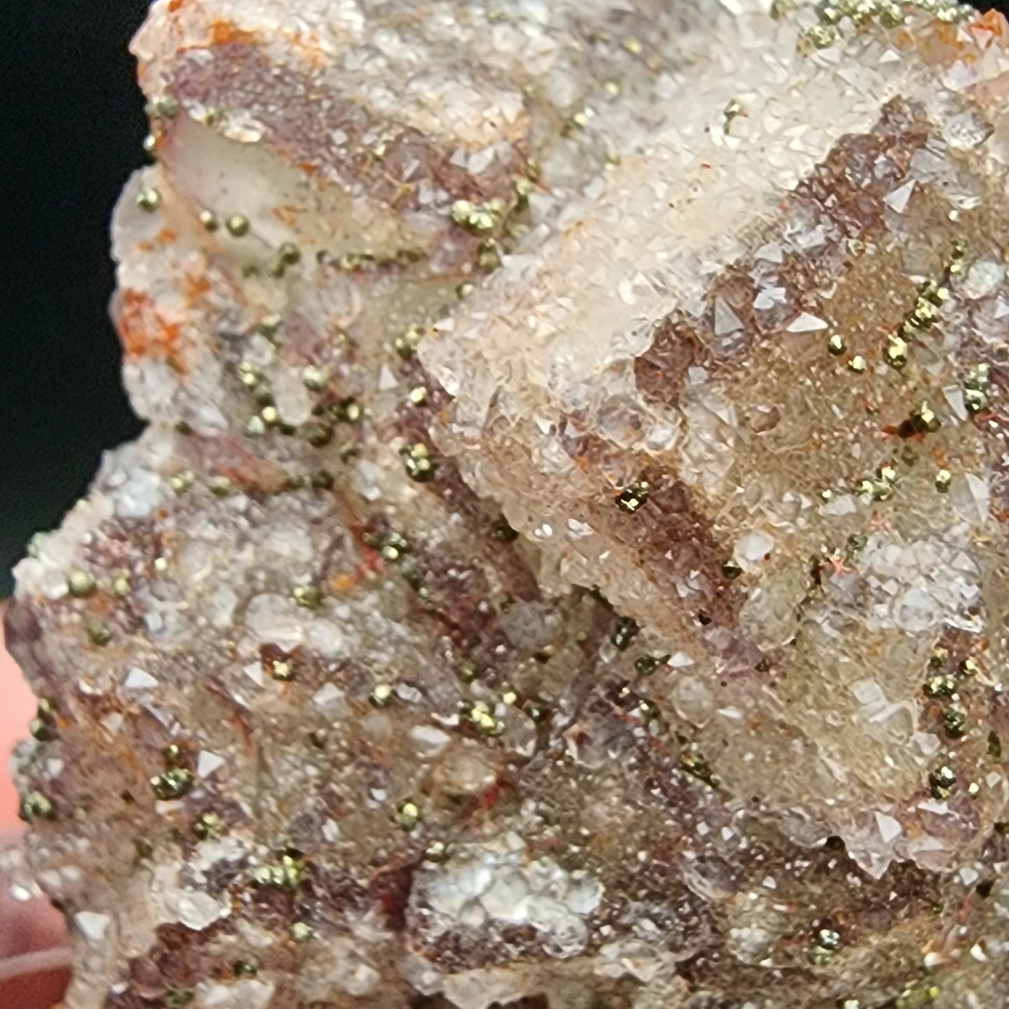 Close-up of an AUCTION Fluorite/Pyrite mineral specimen from The Crystalary, sourced from the Hermine Mine in Lissenthan, Nabburg, Schwandorf District, Upper Palatinate, Bavaria, Germany. The stone showcases a rough crystalline texture with a predominantly clear composition interspersed with white and brown hues. Shades of green are visible as small inclusions or encrustations. Tiny flecks within the dark green background indicate the presence of pyrite, possibly resembling vegetation.