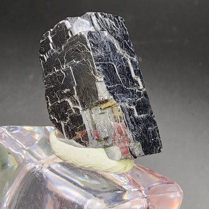 Close-up image of a galena specimen from Missouri's Sweetwater Mine, featuring distinct striations and a shiny surface, displayed on a clear quartz base. The dark, reflective texture of the galena contrasts with the smooth, translucent quartz, creating a striking visual effect reminiscent of high-quality mineral specimens. Available from The Crystalary under the name "AUCTION Galena- Sweetwater Mine, Ellington, Reynolds County, Missouri, USA.