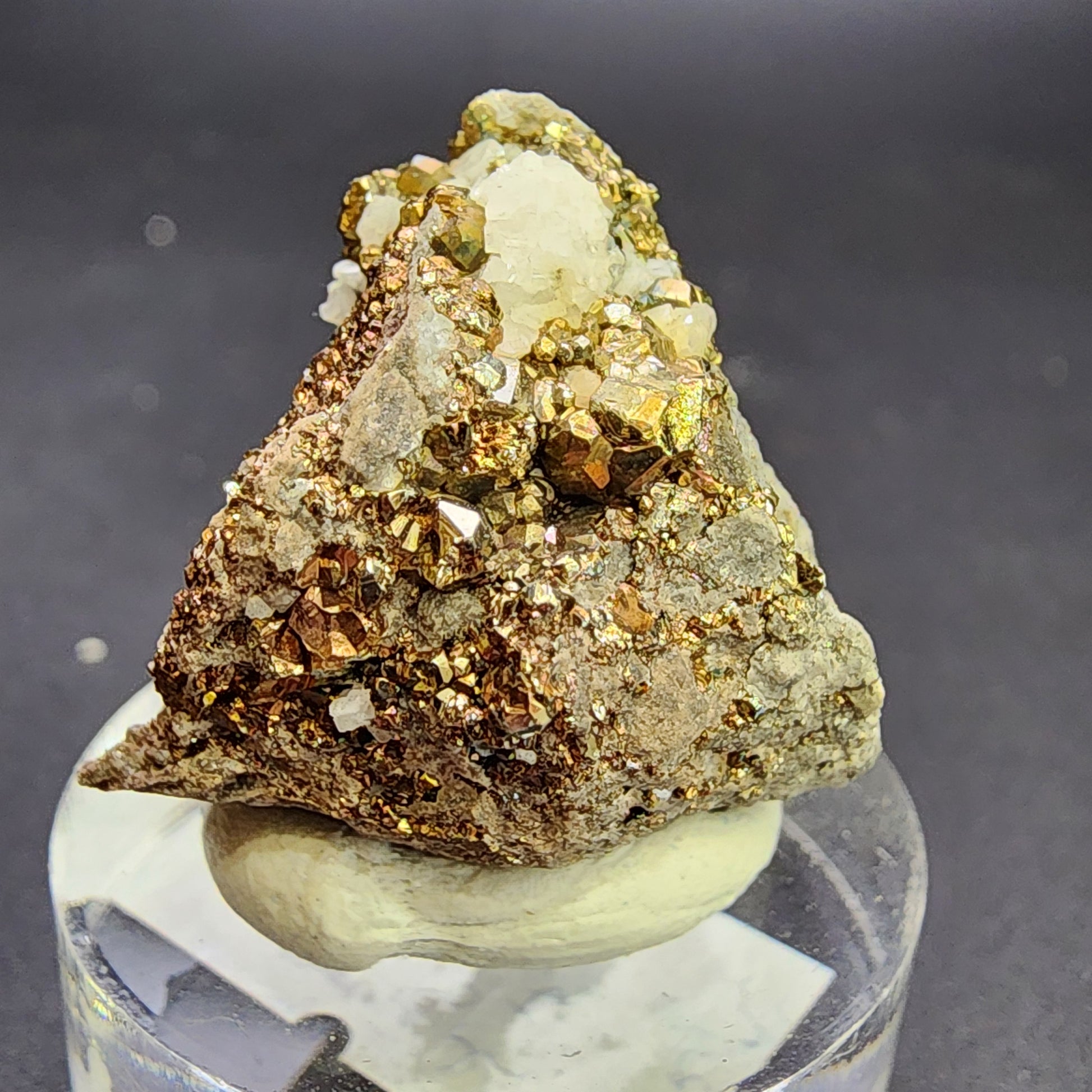 A close-up of a mineral specimen known as AUCTION Pyrite/Dolomite from the C.E. Duff & Son Quarry in Huntsville, Logan Co., Ohio, USA, by The Crystalary. The pyrite crystals, also referred to as fool's gold, exhibit a metallic, gold-like shine with angular geometric shapes embedded in grey rock dolomite. The specimen is displayed on a small circular pedestal against a dark background.