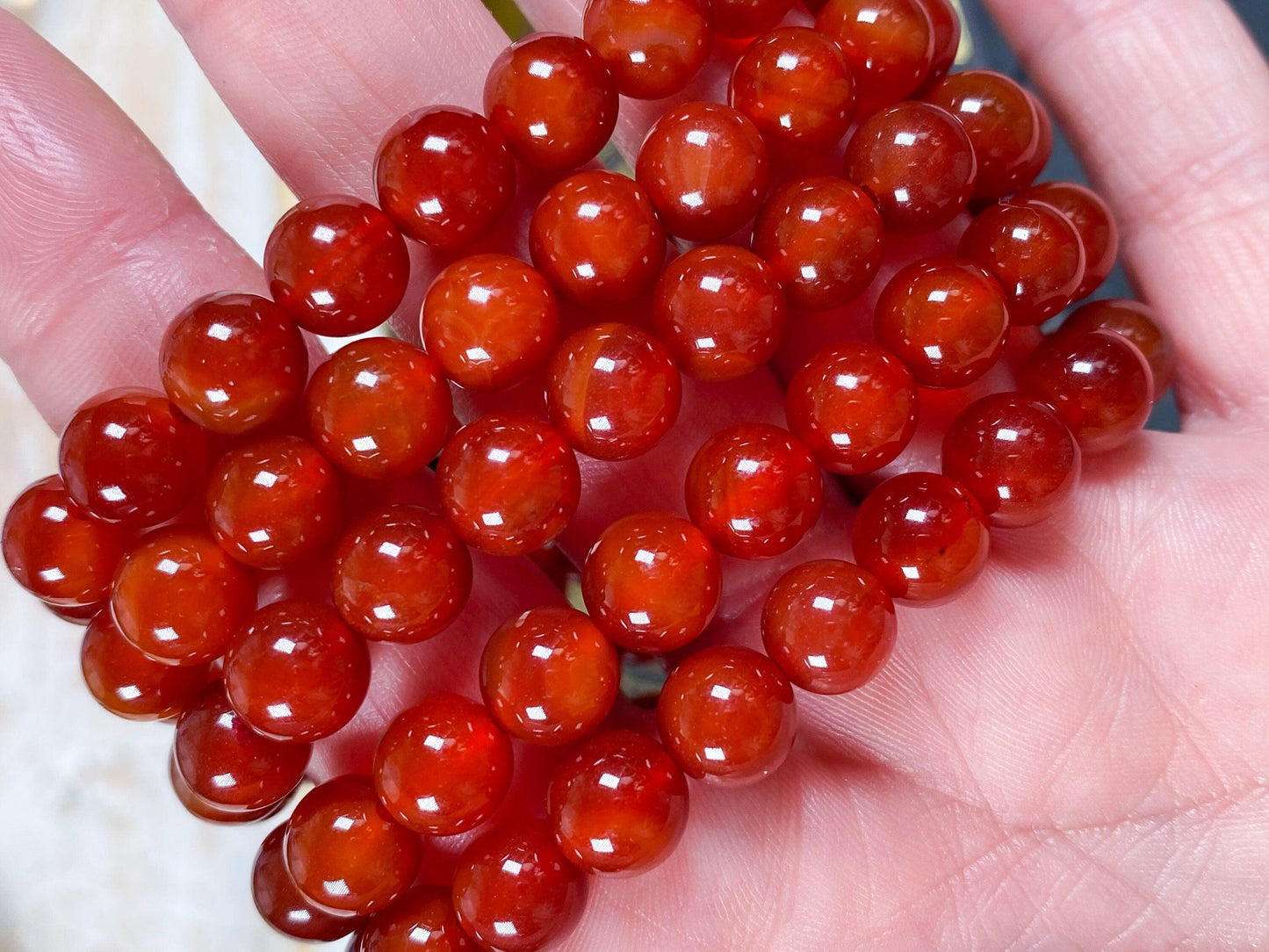 A close-up of two Carnelian Crystal Bracelets by The Crystalary held in a person's hand. The round, shiny beads vary in shades of rich amber colors, from deep red to warm orange. The polished appearance highlights each bead's width, making the smooth surface reminiscent of elegant Carnelian jewelry.