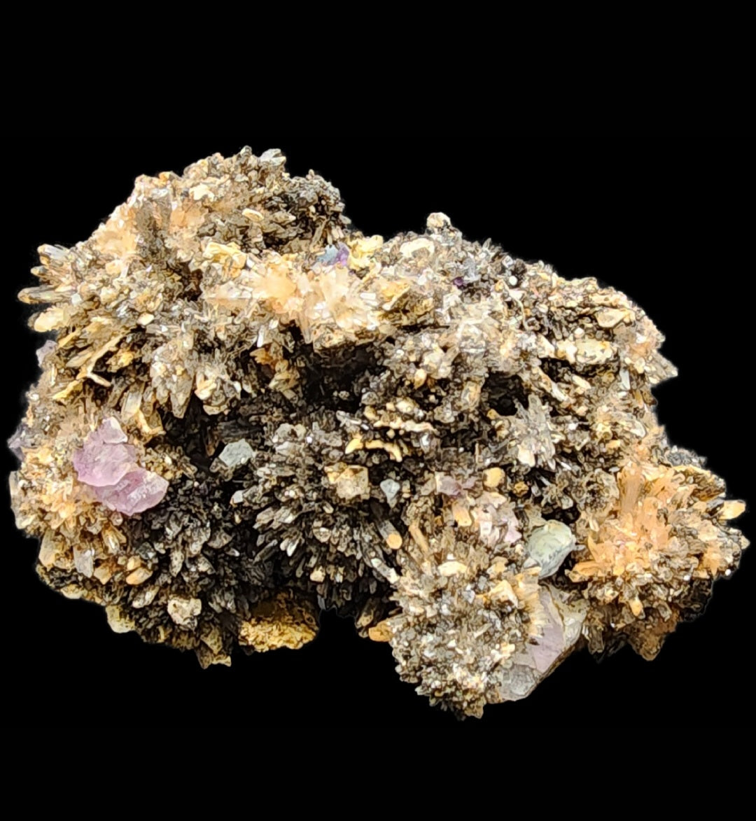 A detailed image of a mineral cluster featuring numerous small, spiky crystal formations. The crystals, including vibrant spiky orange creedite and hints of high fluorescence purple fluorite, vary in color with shades of yellow and brown, set against a plain black background. This stunning formation hails from the Navidad Mine in Inde Municipality, Durango, Mexico, and is offered by The Crystalary under the product name "Creedite Fluorite.