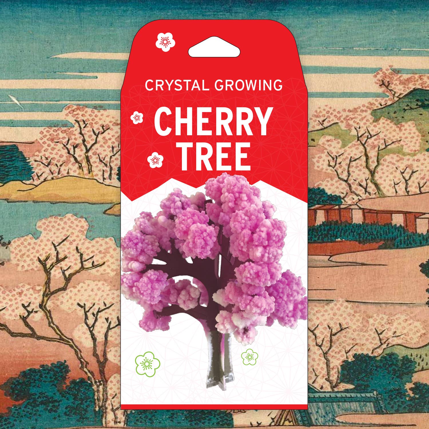 A packaged DIY kit labeled "Crystal Growing Cherry Tree" from Copernicus Toys is displayed in front of a traditional Japanese-style painting featuring cherry blossom trees and rural buildings. This craft and science kit showcases an example of the finished product, a small pink crystal tree.