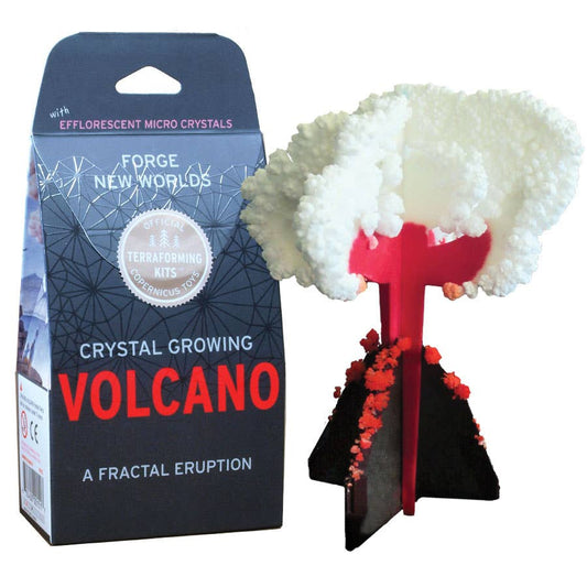 A boxed craft and science kit labeled "Crystal Growing Volcano | Craft Kit Science Kit" by Copernicus Toys features a miniature erupting volcano model beside it. White crystalline structures, resembling smoke and ash, emerge from the red and black base. This intriguing science gift is perfect for curious minds.