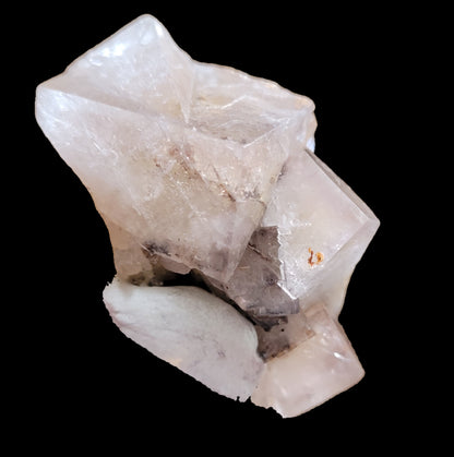 A close-up image of a light-colored crystal cluster, possibly Fluorite- Bull Vein from Lady Annabella, Co. Durham, England by The Crystalary, with several transparent and translucent facets featuring some white and gray inclusions. The contrast is enhanced against a solid black background.