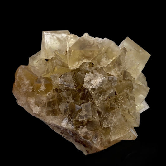 A cluster of translucent, pale yellow cubic crystals from the Fluorite- Bull Vein, Lady Annabella, Weardale, Co Durham, UK by The Crystalary is displayed against a black background. The yellow crystals are tightly packed, forming a rugged yet orderly structure with some edges appearing clearer than others, reminiscent of formations found in mineralized flats.