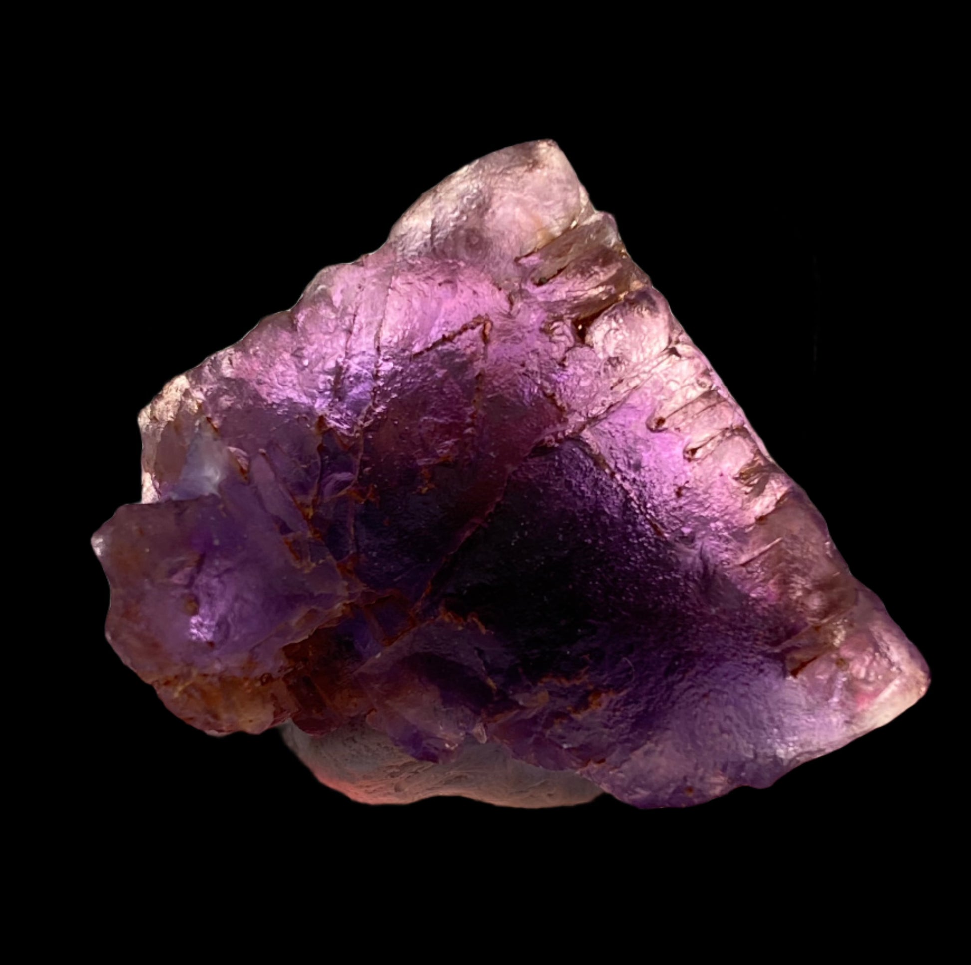 Close-up of a single, rough Fluorite- Cave in Rock from Hardin County, Illinois, USA by The Crystalary, featuring a mix of light and dark purple hues. This specimen showcases an irregular shape and textured surface. Displayed against a solid black background, the gemstone’s translucent quality and natural formations are beautifully highlighted.