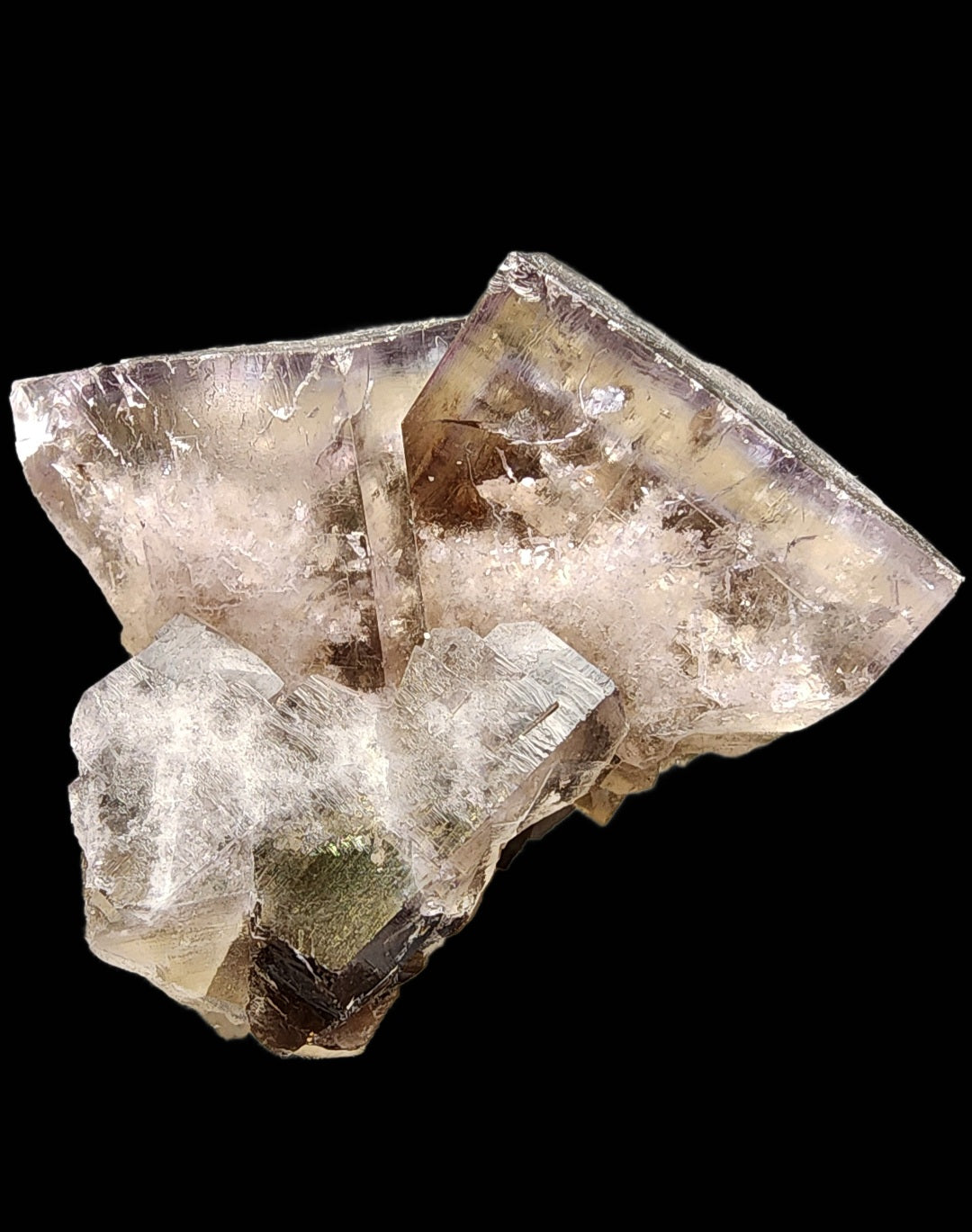 The Cromwell Pocket, available from The Crystalary, features a cluster of translucent fluorite crystals with a pale purple hue against a black background. These crystals from the Greenlaws Mine in Daddry Shield, Stanhope, Co. Durham, England (product number 3077), exhibit zoning with jagged edges and a shiny, reflective surface that beautifully showcases their natural formation and texture.