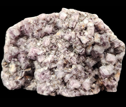 A close-up image showcases the "Fluorite, Funky February" from The Crystalary, featuring an intricate cluster of light purple, slightly translucent cubic crystals sourced from the renowned Greenlaws Mine in Co. Durham, England. The black background accentuates the glassy appearance and natural details of this exquisite mineral.