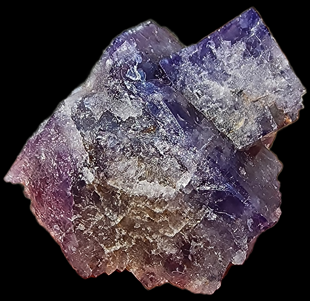 The close-up image showcases a crystalline mineral from The Crystalary's collection, specifically the Fluorite- Purple Haze Pocket from Diana Maria Mine in Rogerley, Weardale, England. The Fluorite displays a rough texture with a beautiful gradient of colors transitioning from deep purple at the top to shades of pinkish-lavender towards the bottom. Its geometric facets are an intriguing mix of transparent and opaque surfaces.