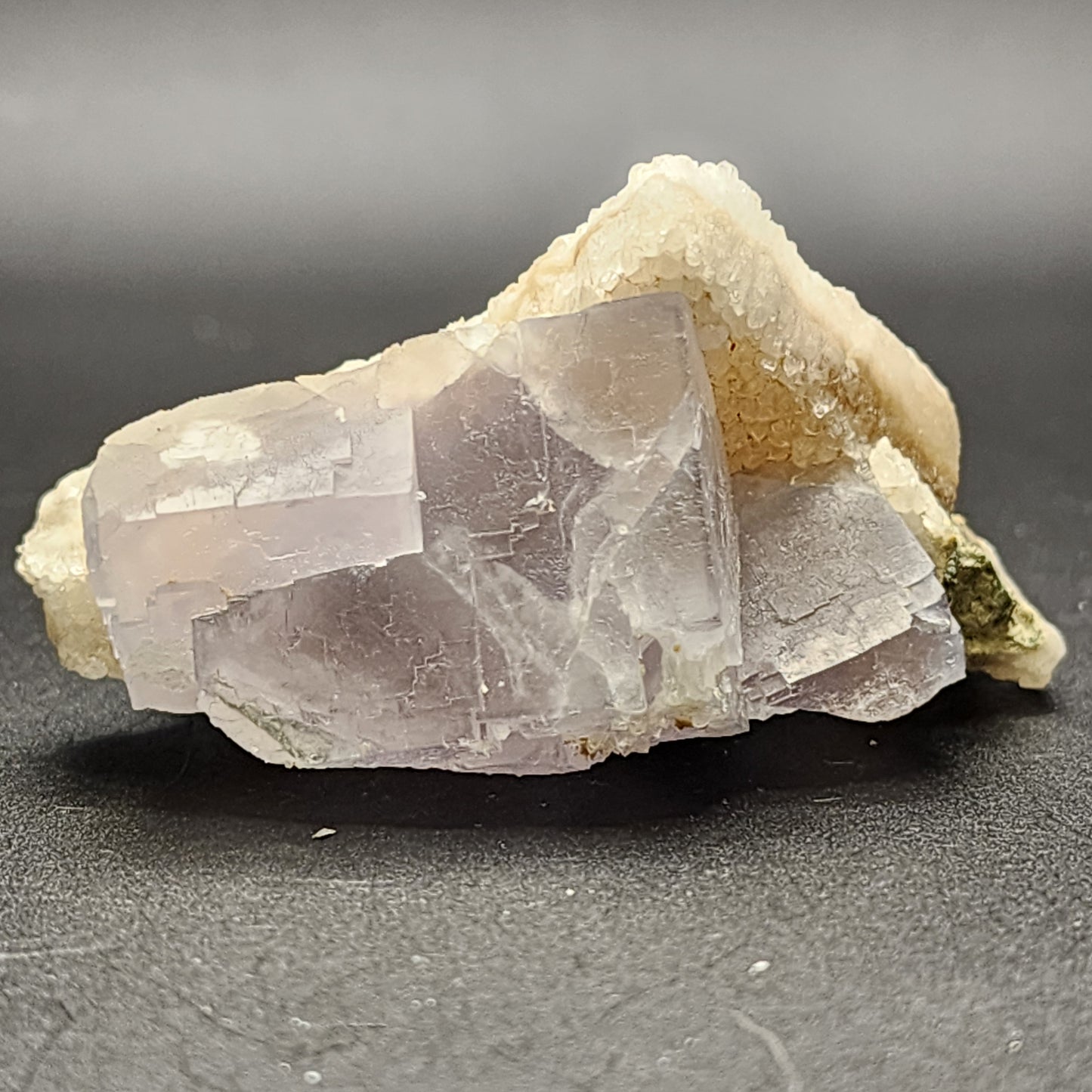 A close-up of a translucent, pale purple crystal set against a soft, dark background showcases its natural, jagged edges and intricate internal patterns, reminiscent of the striking Fluorite from The Crystalary's collection found in the Fishstick Pocket of the Hansonburg District, Socorro County, New Mexico (SKU 5855).