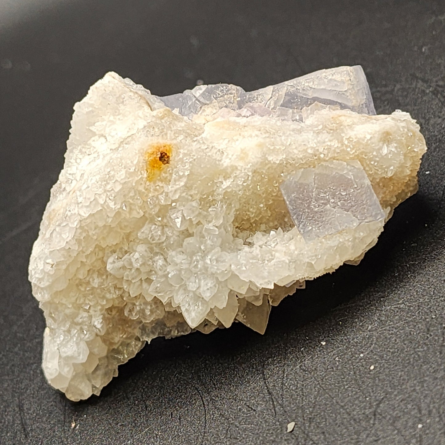 A white quartz crystal formation with angular shapes rests on a black surface, its rough texture sparkling slightly under the light. Nestled beside it is a blue fluorite, part of The Crystalary collection, contrasting beautifully with the quartz's pristine hue and evoking treasures from Fishstick Pocket in Bingham, Hansonburg District of Socorro County, New Mexico.