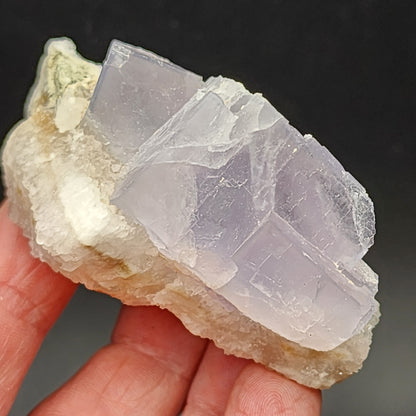 A hand holds a piece of Fluorite and Quartz from the Fishstick Pocket, Bingham in Hansonburg District, Socorro County, New Mexico, crafted by The Crystalary (SKU 5855), against a dark background.