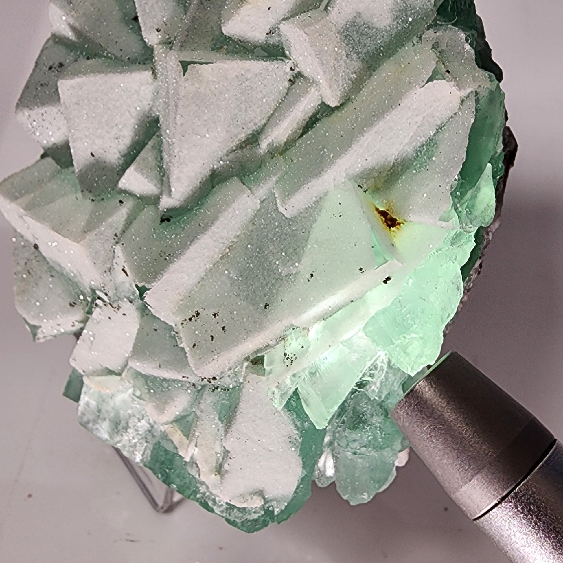 A close-up of a pale green and white Fluorite-Yaogangxian with Mico "Sugar" Quartz mineral specimen from The Crystalary, weighing 248 grams, illuminated from behind by a flashlight. The fluorite crystals are geometric and clustered together, with some areas showing translucence and others appearing more opaque. The background is neutral.