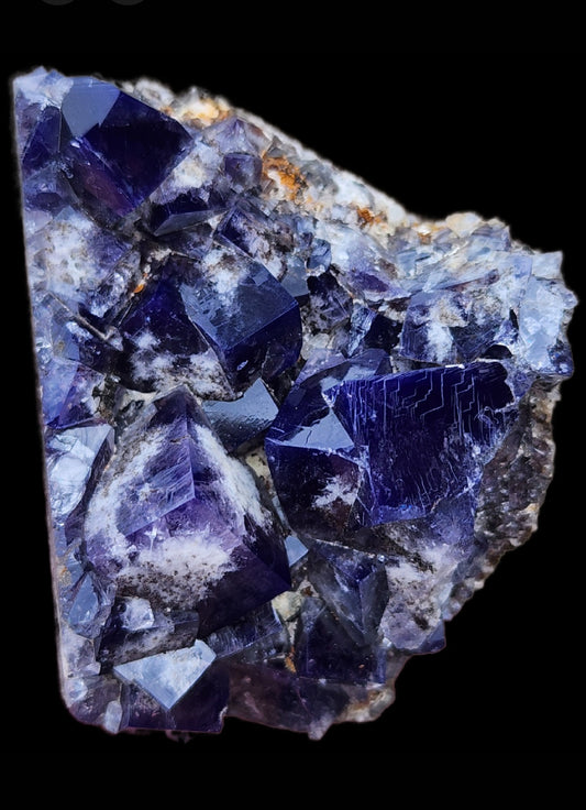 A close-up view of The Crystalary's Fluorite from the Yum Yum Pocket, Diana Maria Mine in Frosterley, Weardale, England reveals a dark blue and purple crystal formation with sharp, angular edges against a black background. The crystalline structure showcases a captivating mix of deep colors and reflective surfaces.