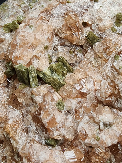 A close-up of the mineral formation showcases translucent, salmon-colored garnet crystals interspersed with clusters of green prismatic diopside crystals. The texture appears rough and intricate due to the varied crystal sizes and shapes, reminiscent of the renowned formations found at Jeffrey Mine. Available from The Crystalary, this stunning piece hails from Val-des-Sources, Les Sources RCM in Estrie, Québec, Canada.