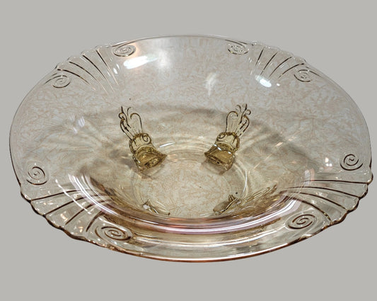 A transparent, textured glass serving bowl with a subtle floral pattern. The HEISEY Empress Sahara bowl from The Crystalary features elegant, raised swirls along the rim, creating a decorative and delicate design. This RARE yellow glass bowl from the 1940s resembles Heisey Elegant Glass and its plain background highlights its intricate details beautifully. It stands on four dolphin-shaped feet for added elegance.