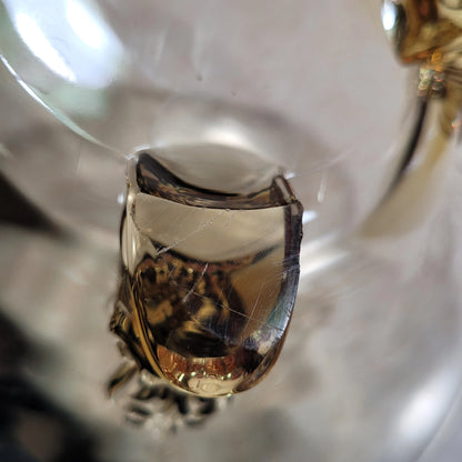 Close-up of a broken piece of transparent glass with visible cracks. The image shows the jagged edges and intricate internal fractures, akin to those found in a HEISEY Empress Sahara 4 footed dolphin foot bowl yellow from the 1940s by The Crystalary, highlighting the reflective and refractive qualities of the material.