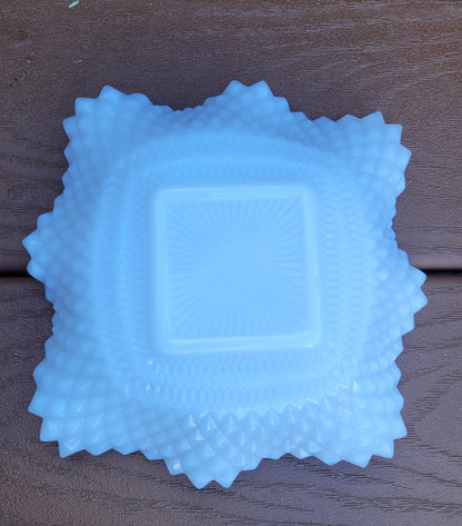 An Indiana Glass Diamond Point Ruffled Candy/Trinket Dish from The Crystalary, featuring a sunburst pattern in the center and a textured, jagged edge, sits on a brown wooden surface, reminiscent of vintage dishes.