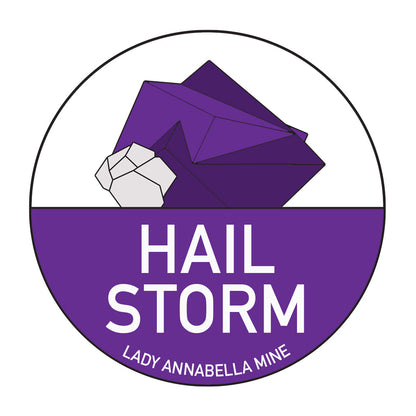 The Lady Annabella Passport Stickers by The Crystalary feature a circular logo with a stylized, full-color purple mineral accented with white highlights. Above the bold, white text "HAIL STORM," "LADY ANNABELLA MINE" is displayed in smaller white capitals below it. The background is divided into sections of white and purple, making it perfect for stickers or as an emblem for your Fluorite Passport.