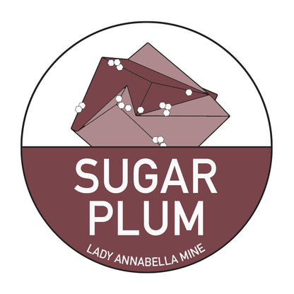 The Lady Annabella Passport Stickers by The Crystalary feature a logo with three stylized brown crystal shapes adorned with white dots on a maroon background. The bottom half of the design showcases a dark maroon semi-circle with "SUGAR PLUM" written in white and "LADY ANNABELLA MINE" below it. Perfect for stickers, its full-color design makes it a standout addition to your fluorite passport collection.