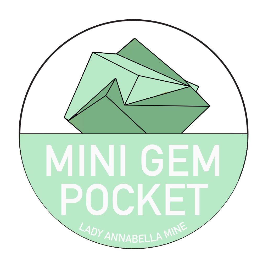 A circular logo features a stylized green gemstone at the center. Below the gemstone, the words "MINI GEM POCKET" are written in bold, uppercase white letters on a light green background. At the bottom, smaller text reads "Lady Annabella Mine" with vibrant Lady Annabella Passport Stickers from The Crystalary adding a splash of full color.