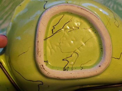 Close-up of the base of a Funky Chartreuse divided serving dish with black crackle lines. The bottom edge reveals an unglazed white ring, showing wear and black marks. A finger is visible on the left side, touching the edge of this mid-century hors d'oeuvre dish handmade in California by Hollywood Ceramics, now available from The Crystalary.