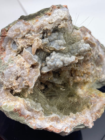 Close-up image of a partially split rock, possibly Millerite, Pyrite, Chalcedony from Halls Gap in Lincoln Co., Kentucky, sold by The Crystalary. It displays a complex, fibrous mineral formation inside. The outer edge is rough and jagged with a mix of white and light brown colors, while the interior reveals thin, hair-like crystal structures of Halls Gap Millerite in a nickel-rich matrix.