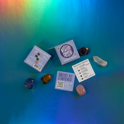 The Mystery Crystal Blind Box Assortment - Stocking Stuffers! by GeoCentral features a set of five healing crystals: amethyst, tiger's eye, black obsidian, clear quartz, and rose quartz. They are elegantly displayed with their blue packaging and informational cards against a vibrant, holographic background—an ideal choice for any Crystal Collection enthusiast.