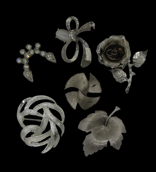 Introducing the Set of 5 Vintage Silver Tone Pins/Brooches Rhinestones Rose Abstract Modern 70s by The Crystalary, intricately displayed on a black background. These brooches, ideal for mix n match styles, feature unique designs including a flower, a leaf, a rose, a bow, and an abstract pinwheel adorned with sparkling rhinestones. Each piece showcases detailed craftsmanship with exquisite patterns.