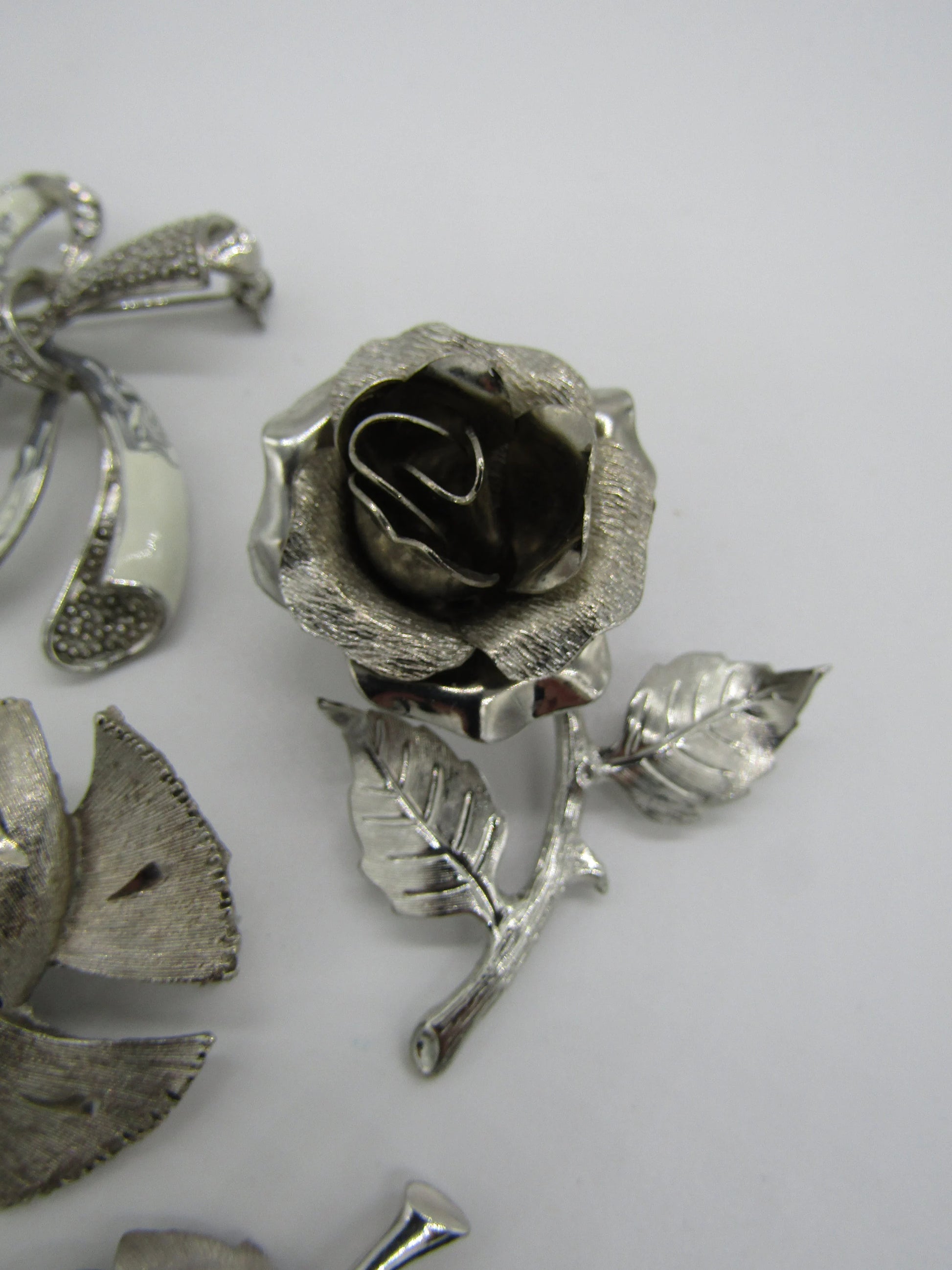 The Crystalary's Set of 5 Vintage Silver Tone Pins/Brooches includes a beautifully crafted brooch shaped like a rose, featuring detailed petals and leaves on a white background. This brooch showcases intricate craftsmanship with textured elements, making it ideal for vintage brooch enthusiasts.