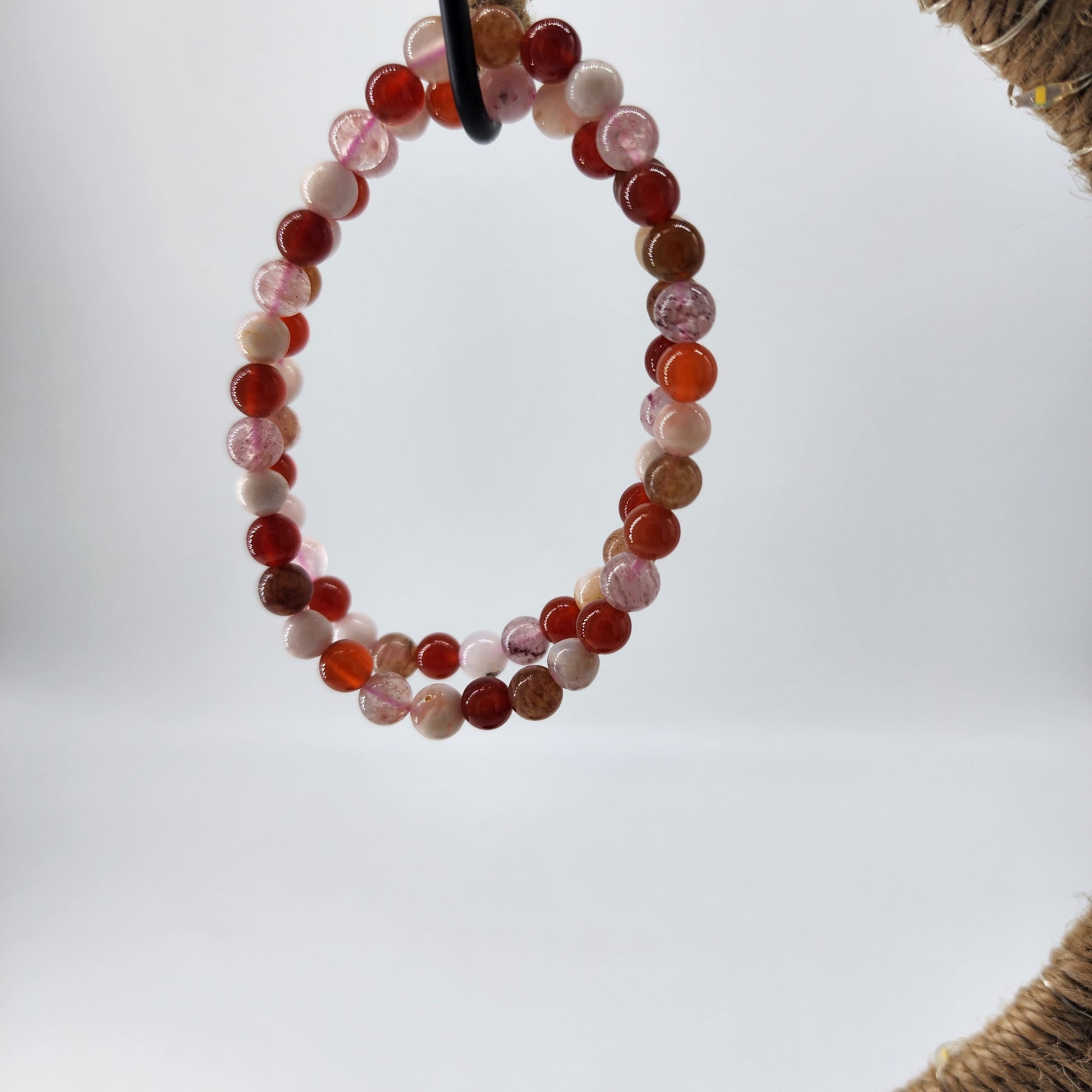 A beautiful round bracelet from The Crystalary, made of Strawberry Quartz, Carnelian, and Flower Agate crystals in shades of red, pink, and white hangs against a plain white background, exuding emotional warmth. The beads have a smooth and polished surface that showcases the creativity behind these stunning bracelets.