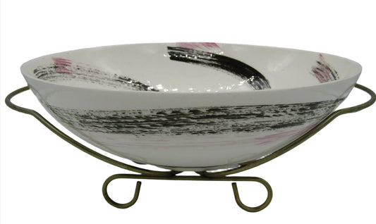 The Wonderful Mid Century California Pottery Bowl with Stand by The Crystalary features a shallow, white ceramic design adorned with kitschy pink and black brushstroke patterns. It sits gracefully on a simple metal stand, showcasing a scroll design at its base. With its slightly curved, oval shape and smooth, glossy finish, this 1950s bowl makes for an ideal decorative piece.